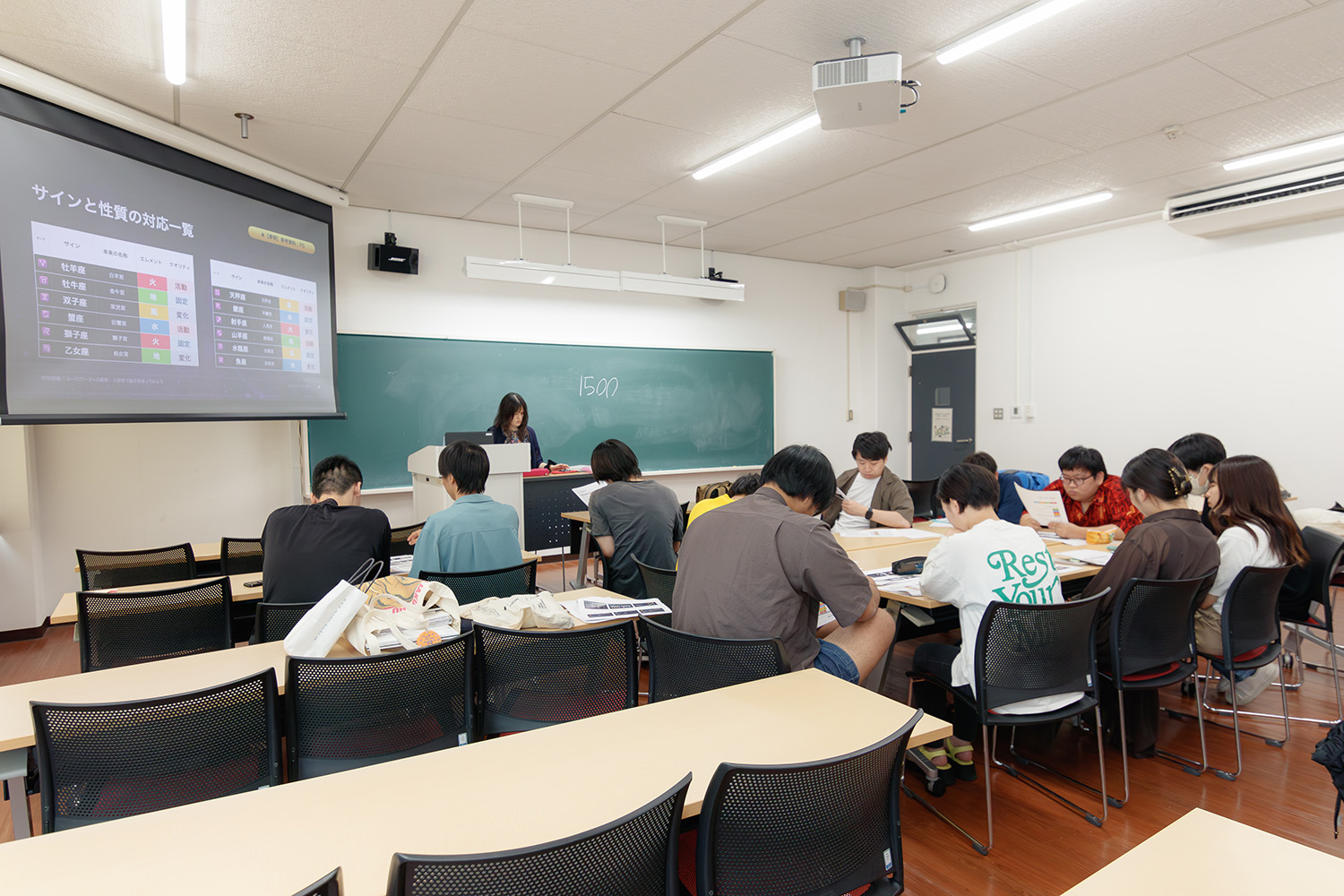 講義会場の遠景　スライドにはサインとエレメント・クオリティの対応一覧が表示されている。受講者は資料を見ながら説明を聞いている。